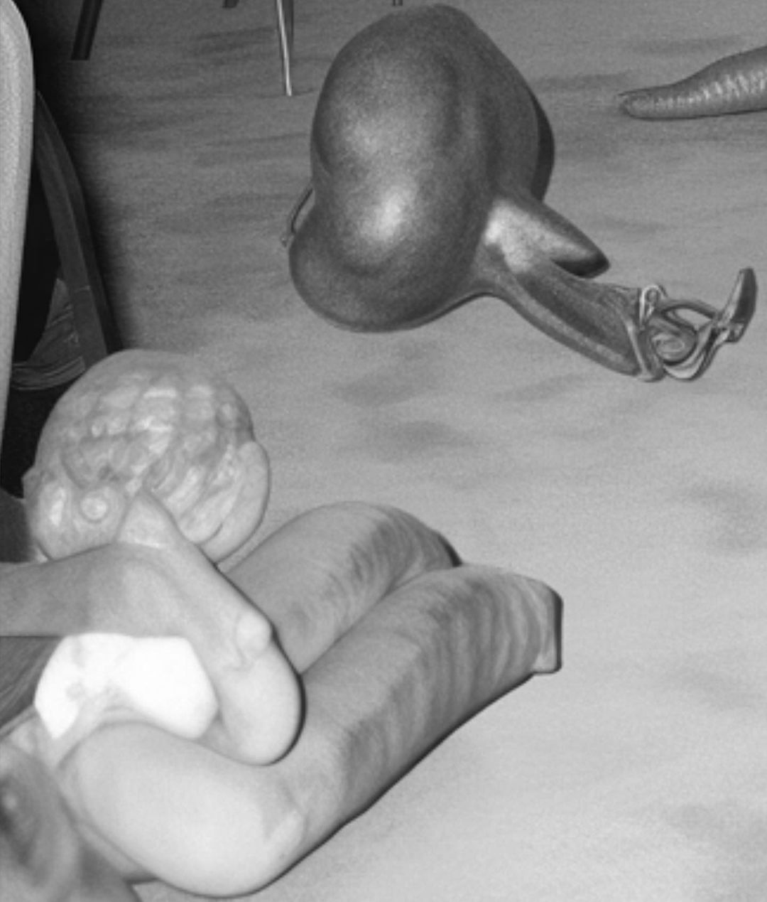 Monochrome image of sculptural forms, including an abstract, bulbous shape and textured, elongated figures, set on a neutral surface.