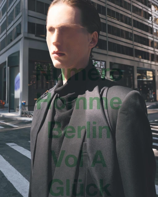 Man in a dark suit stands on a city street in a fashion editorial, featuring modern architecture and natural sunlight.