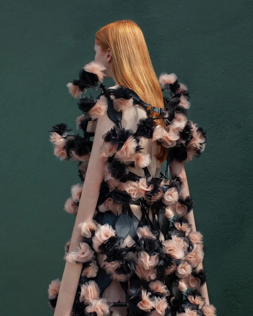 Back view of a woman with red hair wearing a floral dress against a green backdrop, showcasing fashion and editorial style.