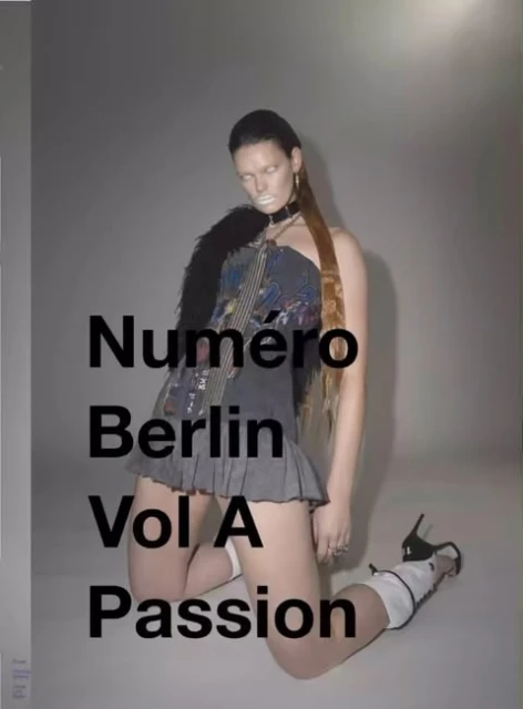 Fashion photo of a woman kneeling in heels, wearing a dark strapless top, grey skirt, and fur stole. She's posed against a grey background.
