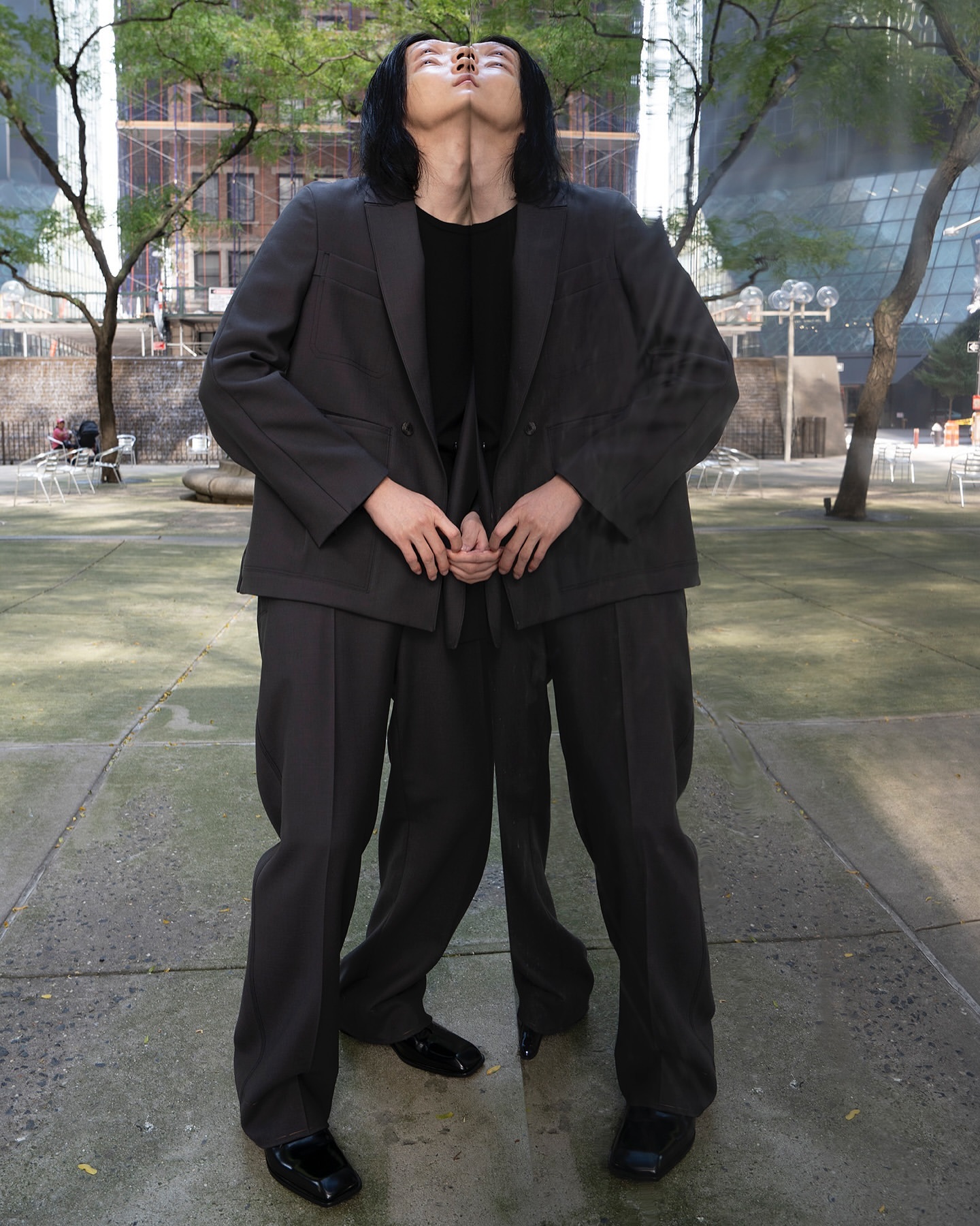 Symmetrical outdoor shot featuring an adult with black hair wearing a dark suit on concrete, creating a mirrored effect in an urban setting.