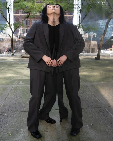 Symmetrical outdoor shot featuring an adult with black hair wearing a dark suit on concrete, creating a mirrored effect in an urban setting.