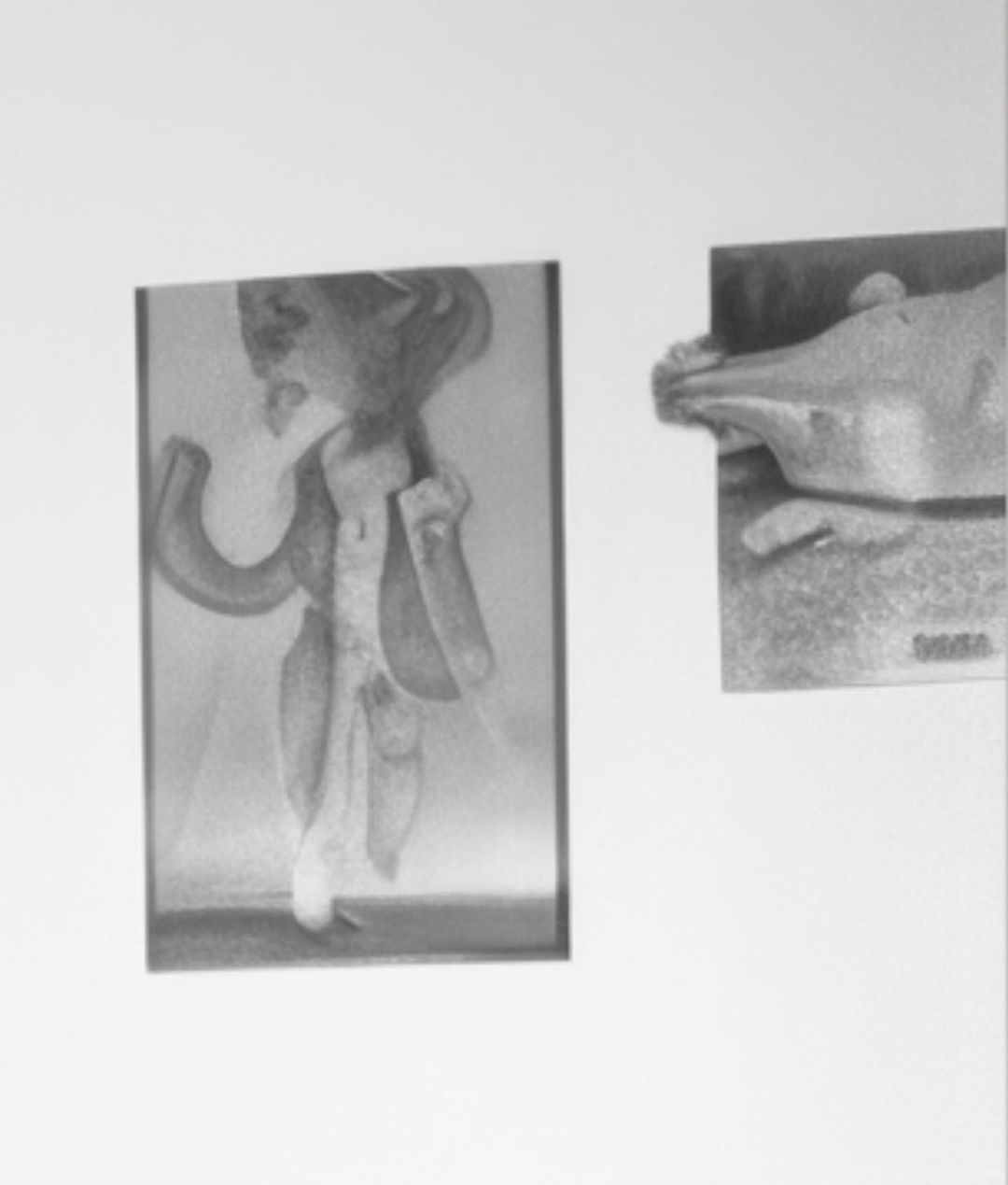 Monochrome artworks on a white wall, featuring an illustration in a black frame and a small, bas-relief sculpture mounted on a panel.