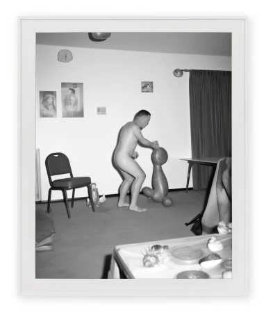 Monochrome photograph by Asger Carlsen featuring a nude man standing in an interior space near an abstract sculptural object.