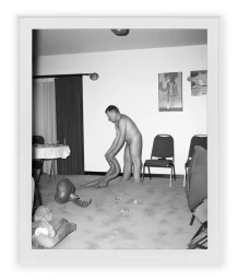 Black and white photograph of a man bending over in an interior room with chairs, a table, and surreal distorted body parts on the floor