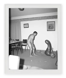 Monochrome photograph by Asger Carlsen of a nude man standing in a living room beside an abstract form