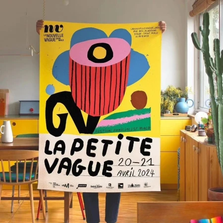 Person holding a vibrant yellow poster with bold abstract graphics and event details in an indoor setting with yellow cabinets.