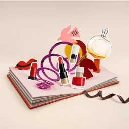 Pop-up book illustration featuring cut-out cosmetics, lipstick, nail polish, and perfume bottle by Atelier Bingo