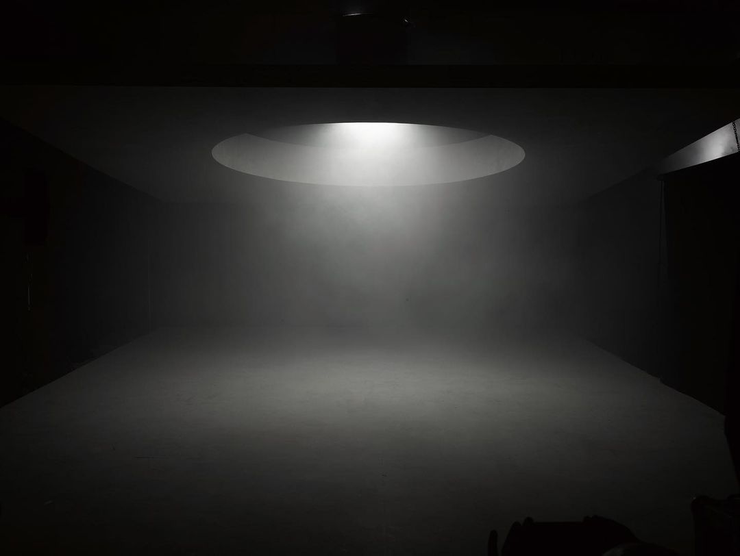 Dimly lit photo studio with a round ceiling light casting a bright beam on the floor, creating a sense of depth and focus.
