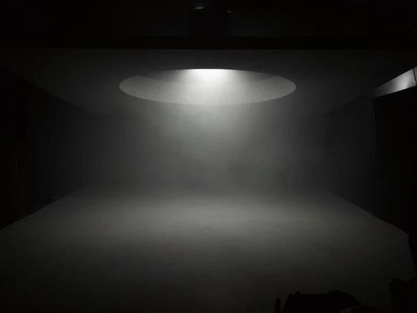 Dimly lit photo studio with a round ceiling light casting a bright beam on the floor, creating a sense of depth and focus.