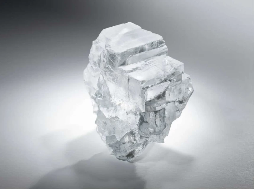 Close-up studio shot of a crystalline mineral specimen on a gray gradient background with a cast shadow showing its cubic structure.