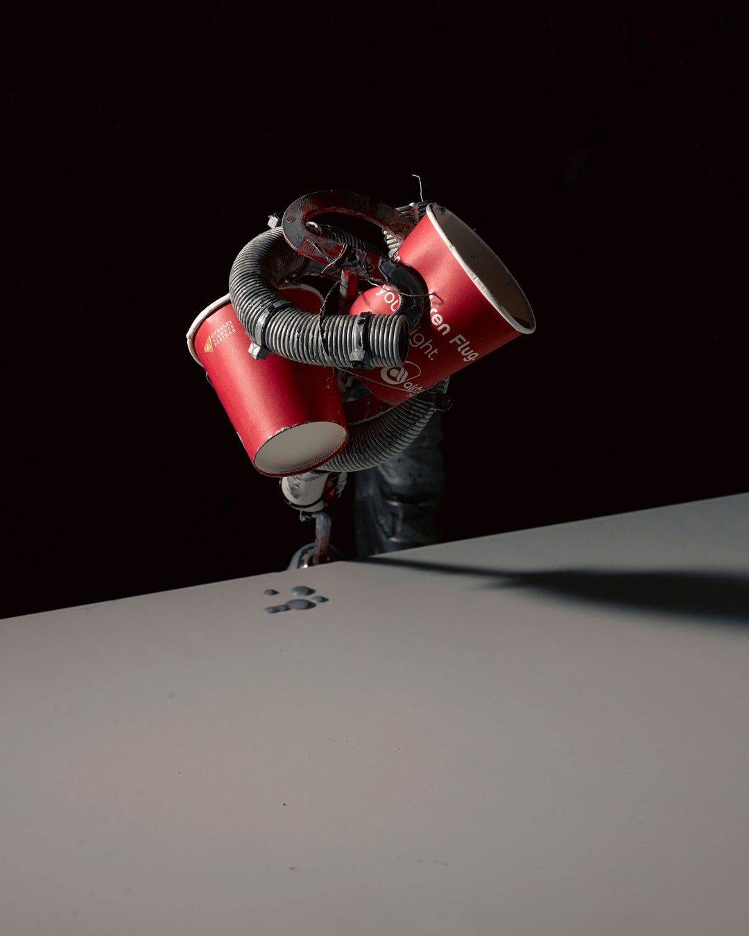 Conceptual studio shot with red disposable cups connected by black tubing against a dark backdrop, highlighted by directed lighting.