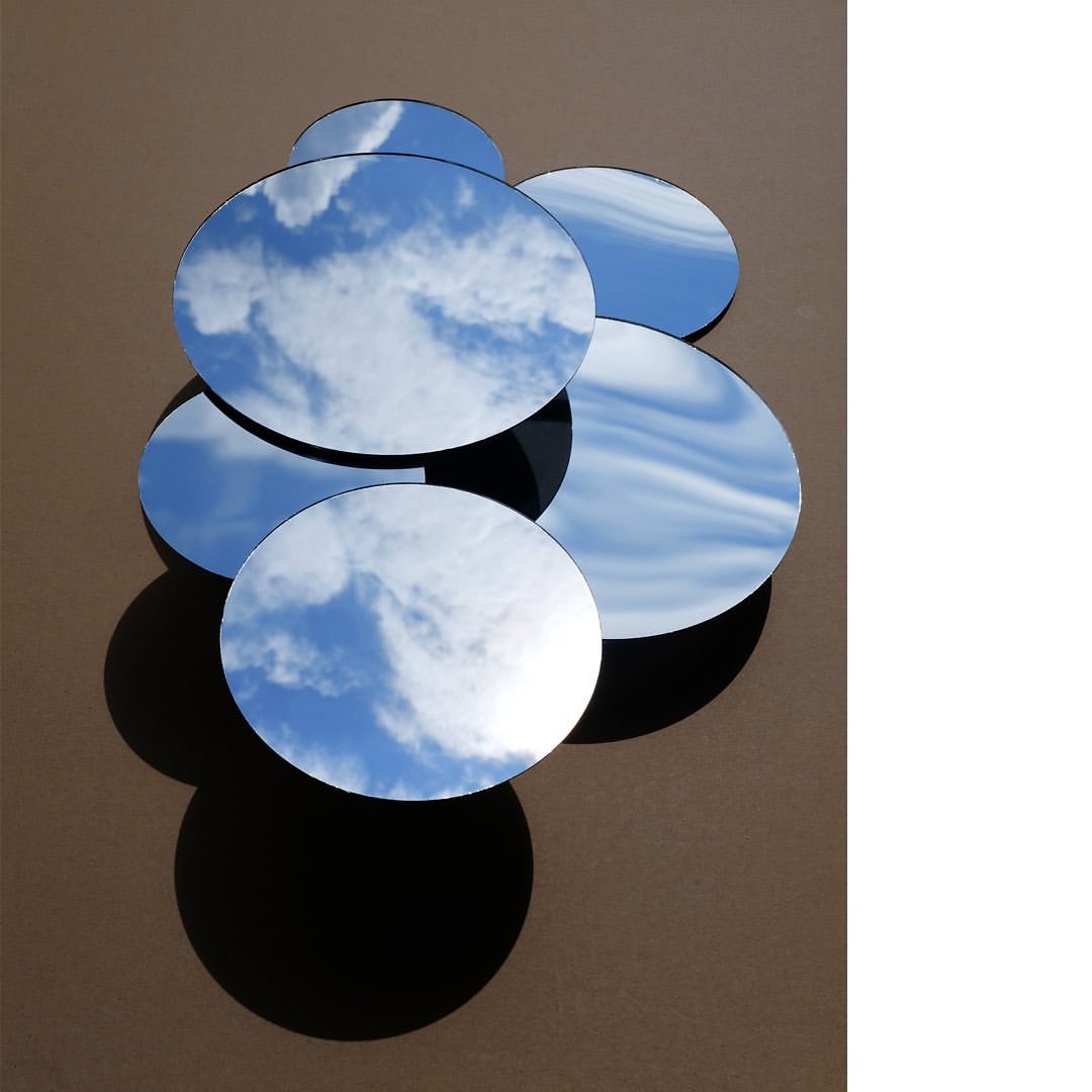 Cloudscape reflecting in a dynamic display of round mirrors against a neutral wall, creating a captivating visual composition and play of light.