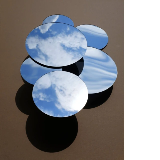 Cloudscape reflecting in a dynamic display of round mirrors against a neutral wall, creating a captivating visual composition and play of light.