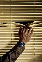 Close-up of a person's hand opening horizontal window blinds wearing a brown shirt and a wristwatch