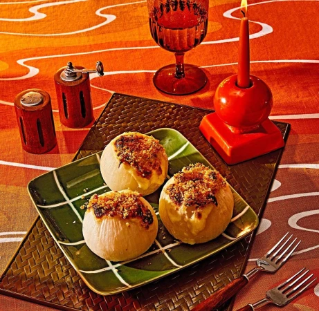 Overhead shot of baked onions with breadcrumbs on a green plate, accompanied by a glass, salt and pepper shakers, cutlery, and a candle.