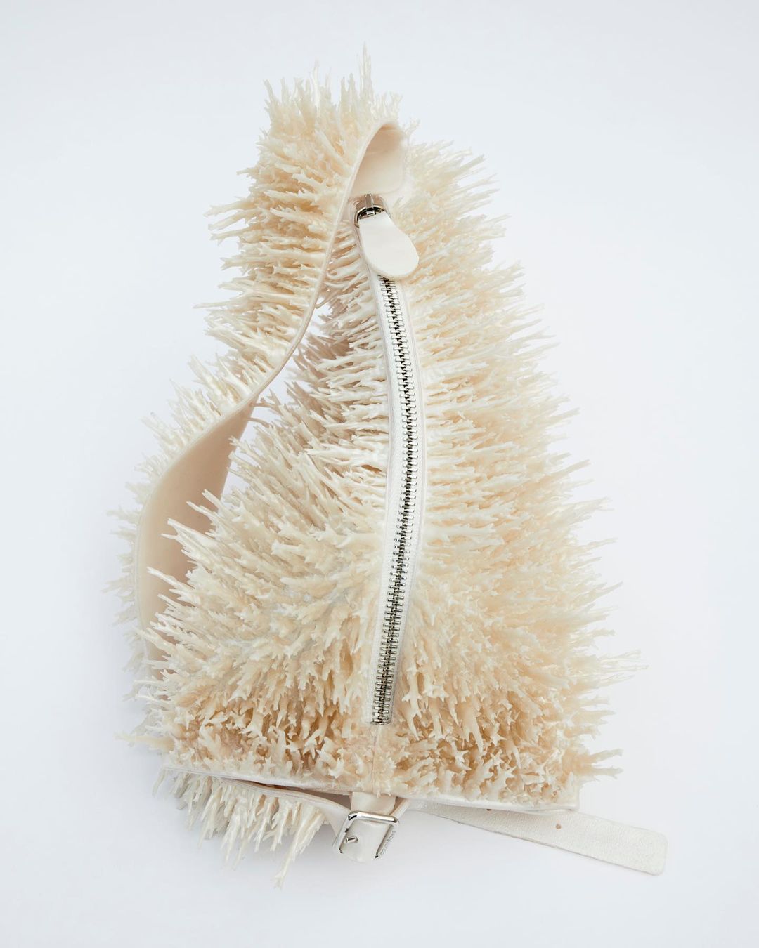 An off-white, textured handbag with a zipper and adjustable strap, set against a plain white backdrop in a studio setting.