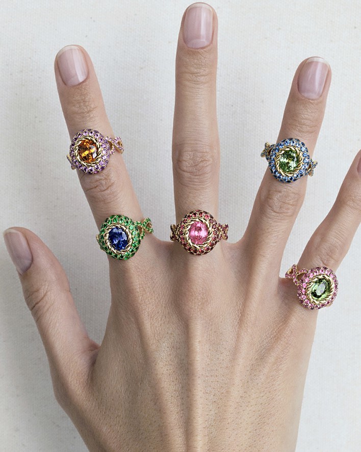 Close-up of a hand wearing five intricate jeweled rings with colorful gemstones on every finger by Aude Le Barbey