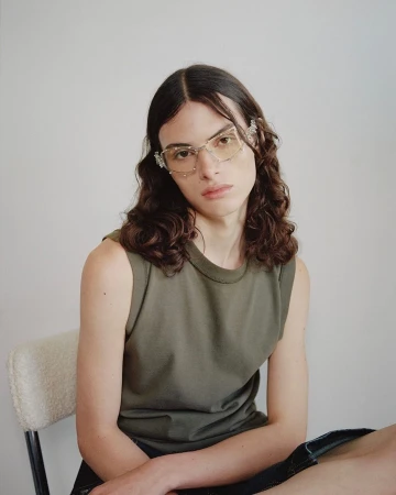 Portrait of a model wearing crystal-embellished glasses and an olive green tank top seated on a chair in Paris by Aude Le Barbey