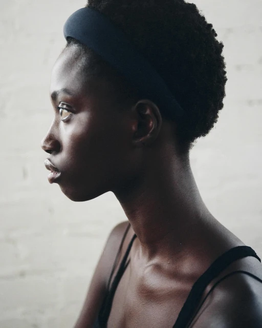 Profile shot of a Black woman with dark curly hair, wearing a headband and tank top against a textured neutral background.