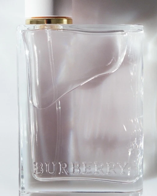 A clear glass Burberry fragrance bottle with a white cap and gold accent is set against a white background in a studio shot.