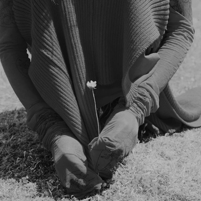 Monochrome image of a person sitting on grassy ground holding a daisy. The composition features natural light and soft textures.