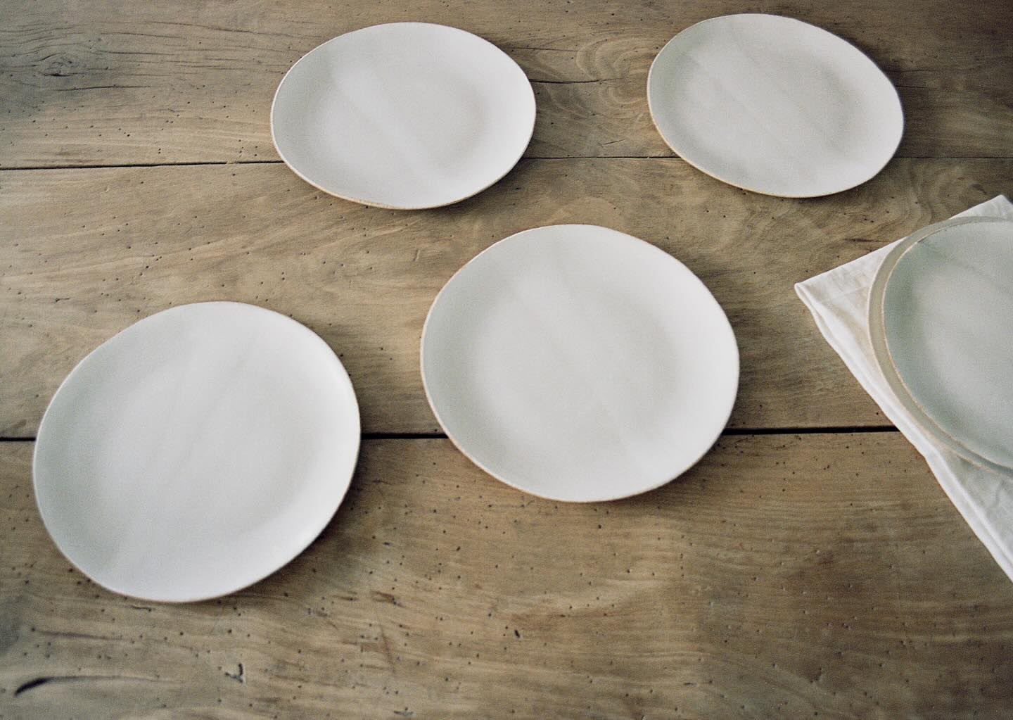 Overhead shot of five white ceramic plates arranged on a rustic wooden table with a linen napkin. Food and beverage photography.