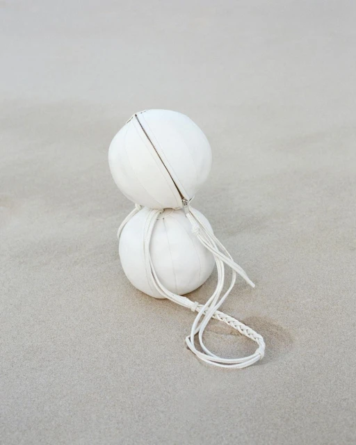 Two stacked white spherical bags with braided cords on a neutral surface. The minimalist image emphasizes texture and round shapes.