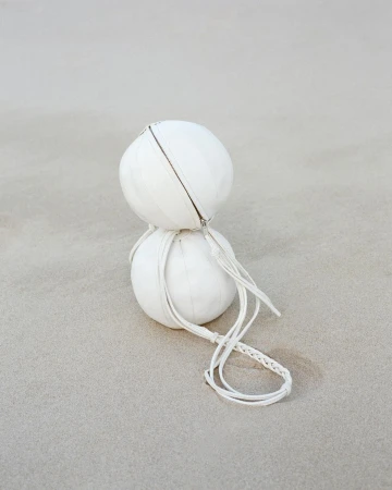 Two stacked white spherical bags with braided cords on a neutral surface. The minimalist image emphasizes texture and round shapes.