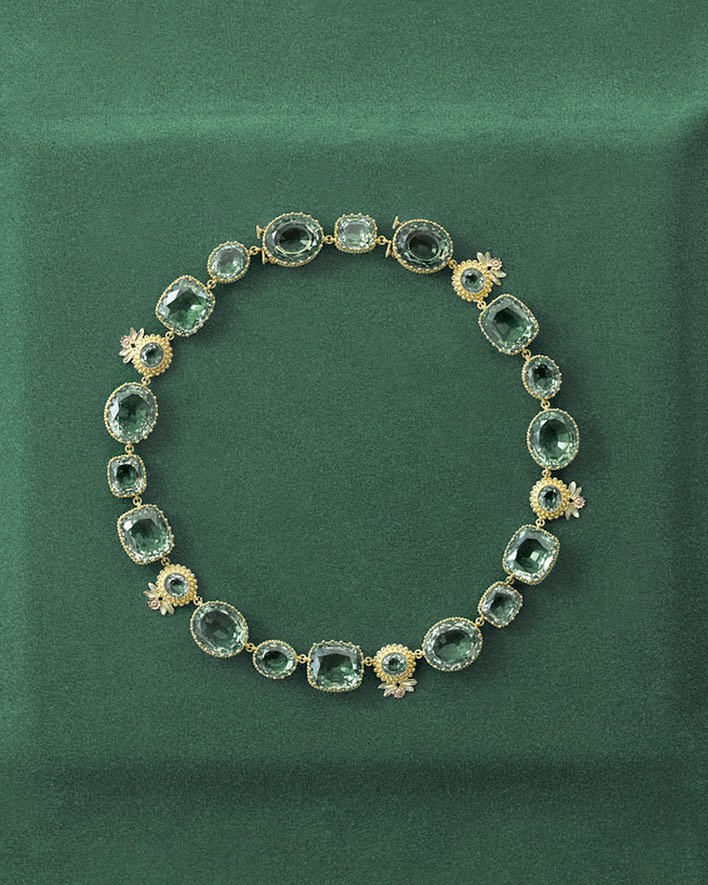 Elegant green gemstone necklace featuring various shapes and sizes of set stones, surrounded by small, ornate floral details.