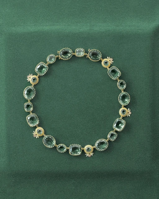 Elegant green gemstone necklace featuring various shapes and sizes of set stones, surrounded by small, ornate floral details.