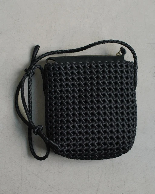 Black woven crossbody bag with a braided shoulder strap on a neutral surface, product photography showing texture and design.