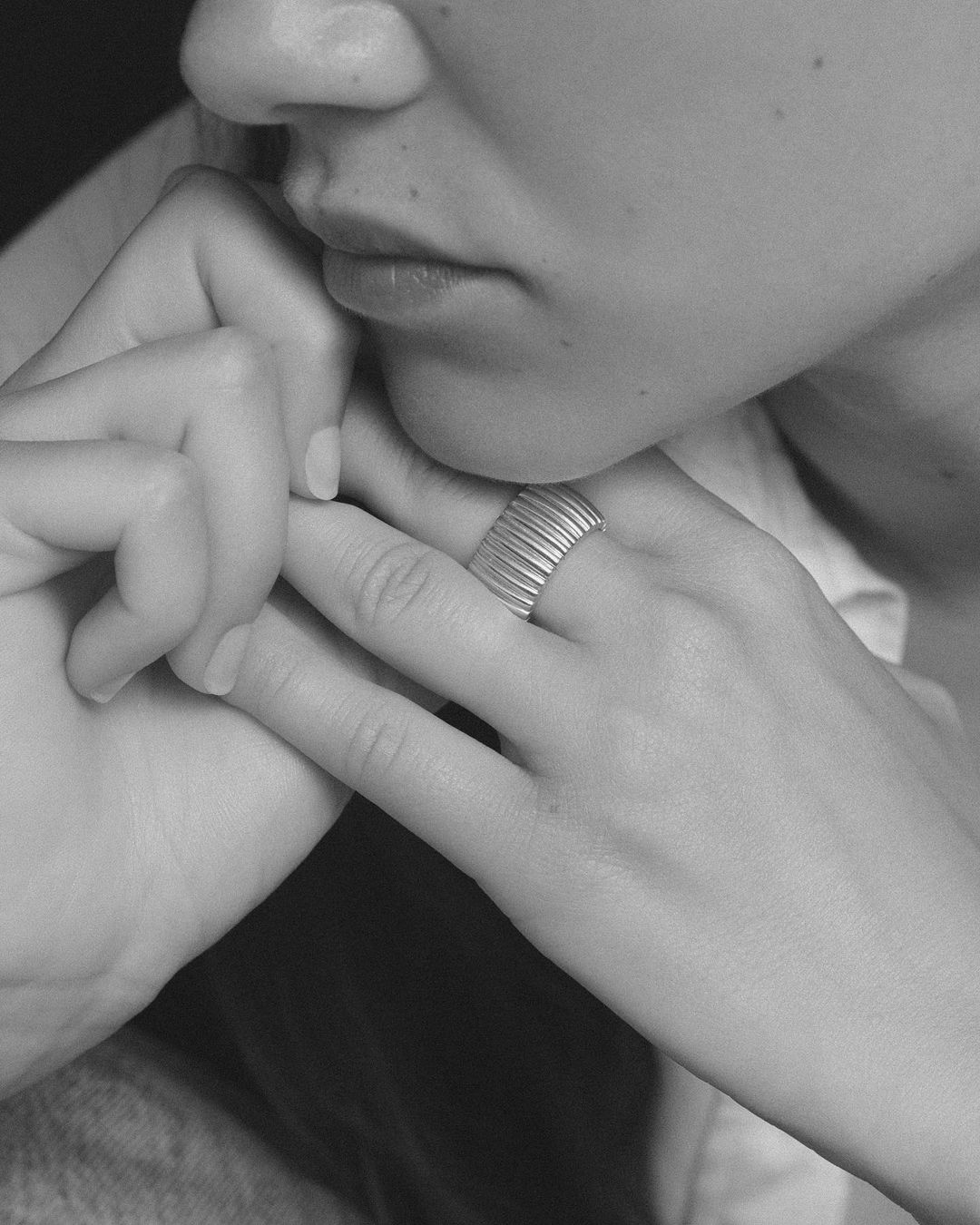 Close-up portrait of a woman resting her chin on her hand, displaying a wide ridged silver ring on her finger.