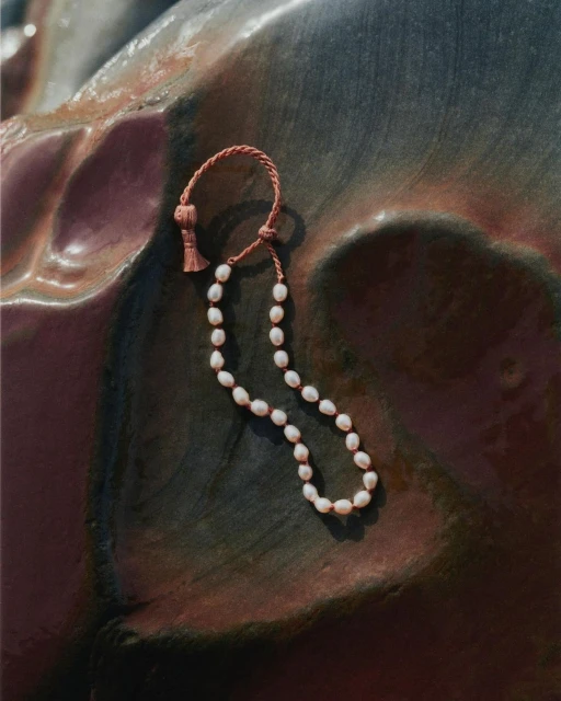 Stylish pearl necklace with a coral-colored cord on a textured surface, jewellery, fashion, and design product shot.