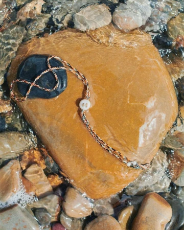 Handmade beaded necklace on a rock in shallow water.  A unique accessory set against smooth stones and rippling water creates an outdoor still life.