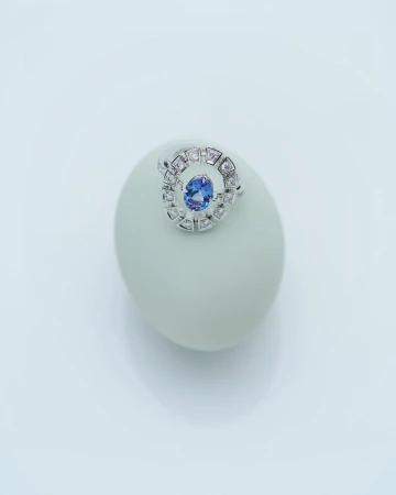 Close-up studio shot of a ring with a blue gemstone set on a white object against a bright white background, creating a clean aesthetic.