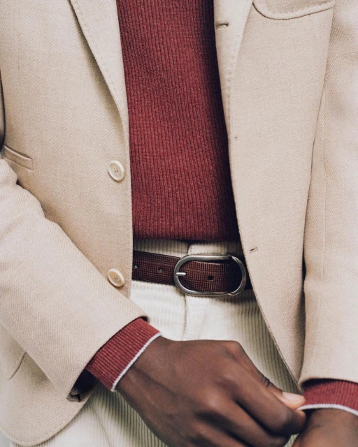 Close-up studio shot of an adult wearing a beige blazer, burgundy sweater, brown belt, and off-white corduroy pants.