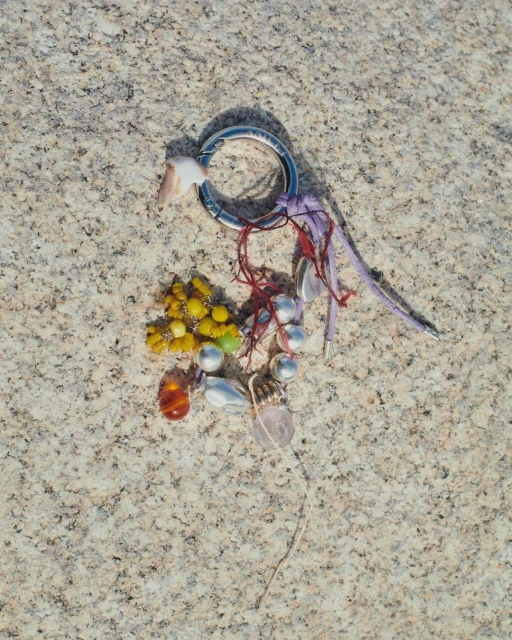 Overhead shot of a handcrafted charm featuring shells, beads, and decorative accents on a textured, light-beige surface.  
