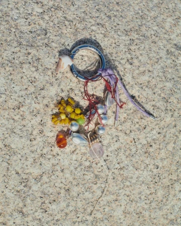 Overhead shot of a handcrafted charm featuring shells, beads, and decorative accents on a textured, light-beige surface.  