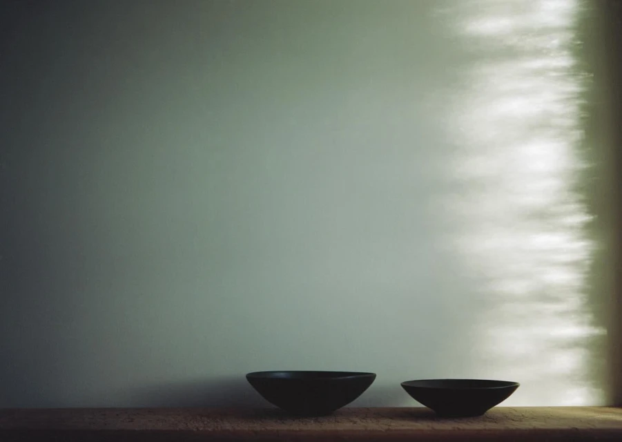 Still life image of two dark ceramic bowls arranged on a wooden surface against a soft grey wall with diffused natural light.