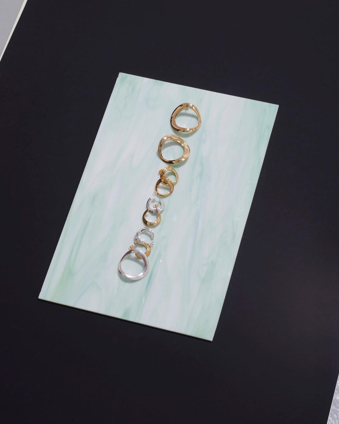Elevated view of a curated arrangement of gold and silver rings displayed on a white surface against a solid black backdrop in a studio setting.