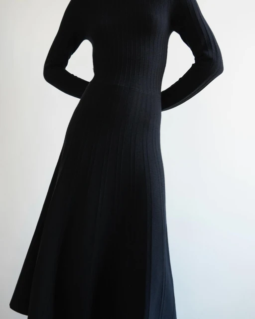 Woman in a long-sleeve black dress with a ribbed texture. The dress flows to mid-calf length against a plain white backdrop.
