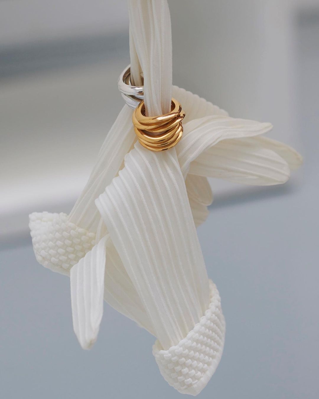Close-up of gold and silver hoop earrings intertwined with gathered white fabric, creating an elegant and textured visual composition.