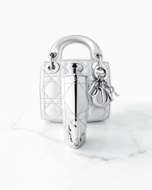 Silver Dior Lady handbag and fragrance bottle on marble surface with a bright background, fashion and beauty editorial product shot.