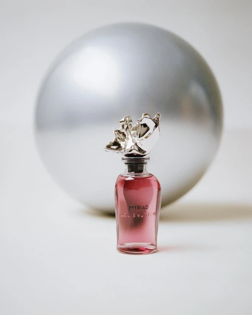 Louis Vuitton perfume bottle, Myriad, with silver decorative stopper against blurred silver sphere, product shot, beauty, indoors.