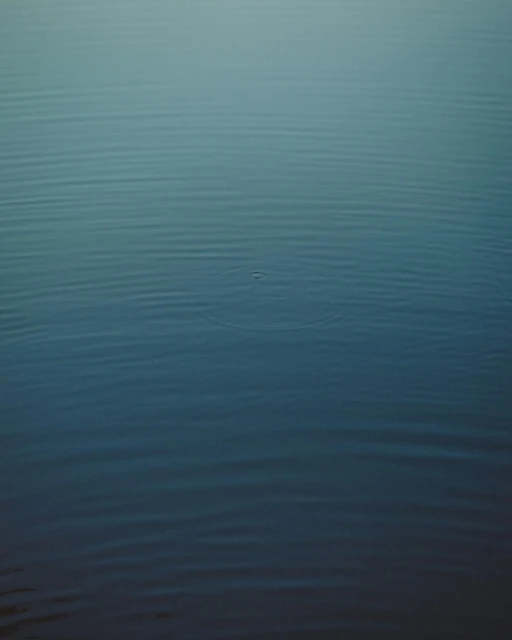 Calm, still body of water showing subtle wave patterns with a gradient of blue shades from dark to light, emphasizing tranquility.