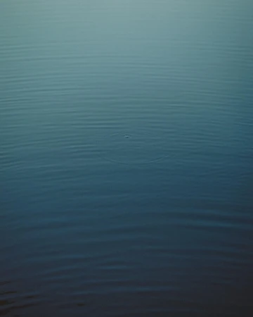 Calm, still body of water showing subtle wave patterns with a gradient of blue shades from dark to light, emphasizing tranquility.