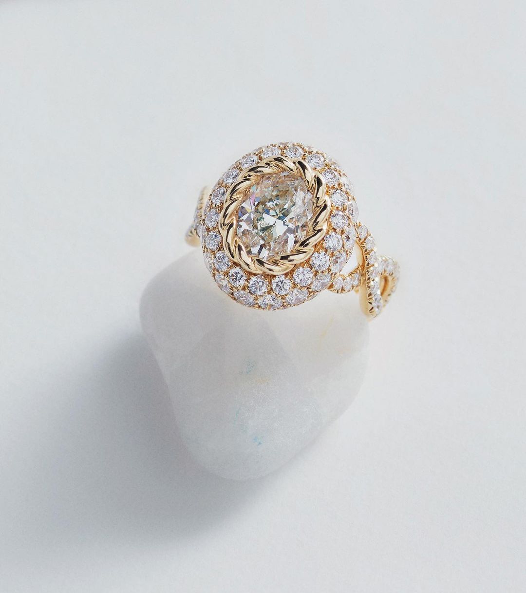 Close-up of an elegant gold ring featuring a central diamond surrounded by smaller diamonds, set on a white stone surface.
