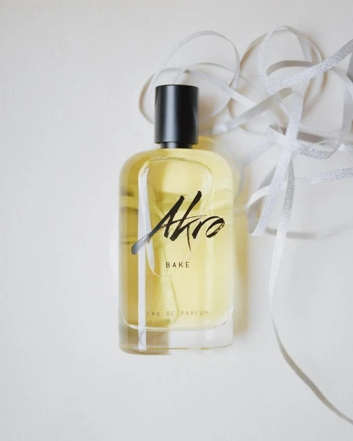 Still life studio shot of an Akro Bake perfume bottle against a white background with a decorative silver ribbon.