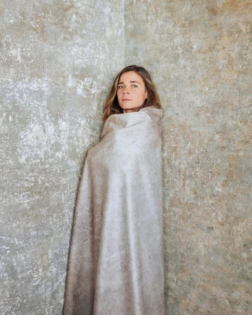 Woman wrapped in a neutral fabric standing in a corner against a textured concrete wall by Audoin Desforges in Paris.
